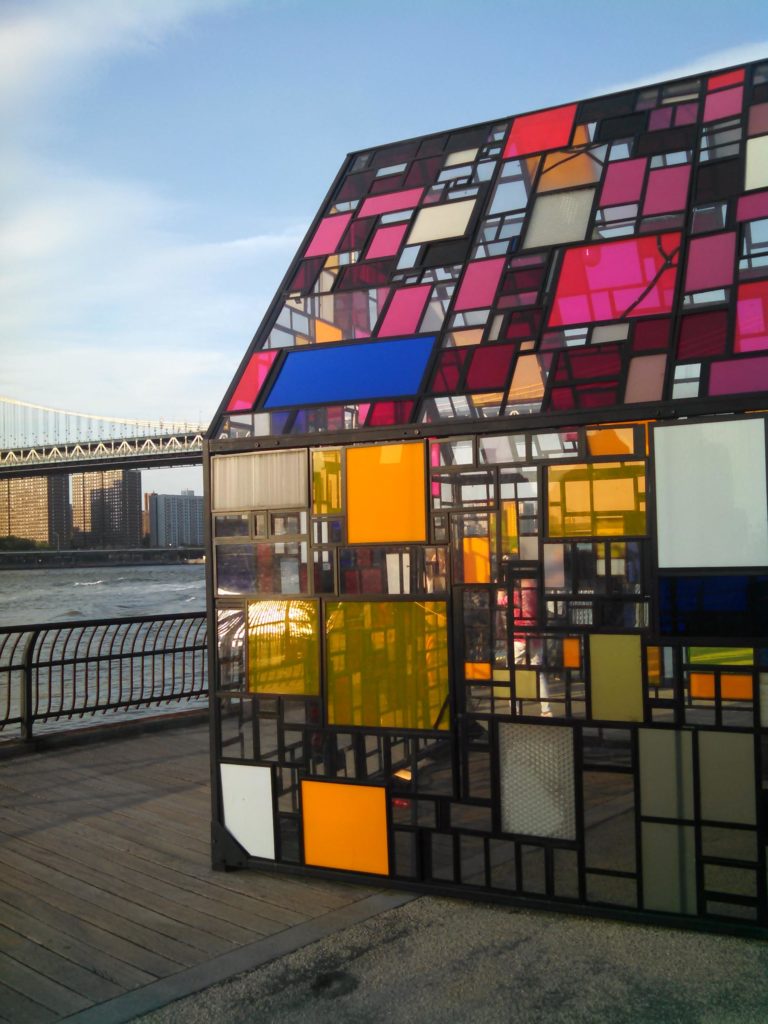 Brooklyn, NY, USA May 25, 2015 A stained glass sculpture, Kolonihavehus by Tom Fruin sits in Brooklyn Bridge Park, overlooking the East River and Manhattan